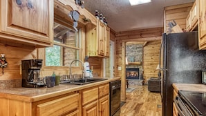 A wooden cabin-style kitchen with a stone fireplace, wooden cabinets, and a black refrigerator. - Whispering Oaks - Private Pigeon Forge Getaway...close To Tanger Outlet Shopping 2 Bedroom Cabin by RedAwning (Sevierville)