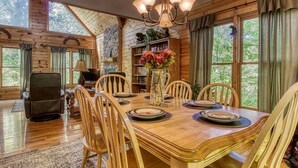 A wooden dining room with a large table, chairs, a chandelier, and a bookshelf filled with books and decorative items. - Whispering Oaks - Private Pigeon Forge Getaway...close To Tanger Outlet Shopping 2 Bedroom Cabin by RedAwning (Sevierville)