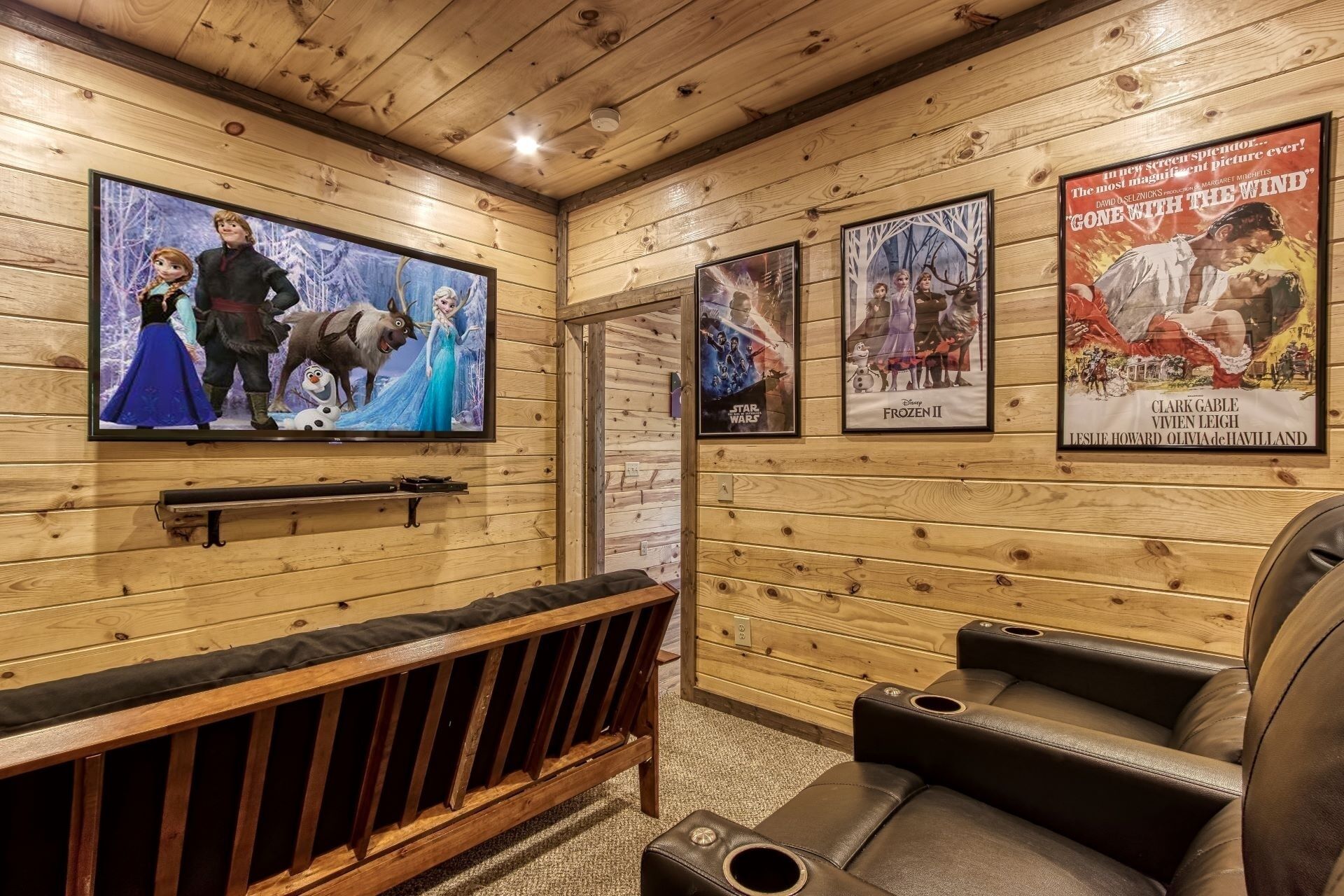 A cozy room with a wooden interior, a flat-screen TV, posters on the wall, a bench, and leather chairs.