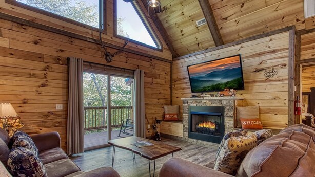 Un intérieur de chalet chaleureux avec une cheminée, des sièges confortables et un grand écran de télévision.