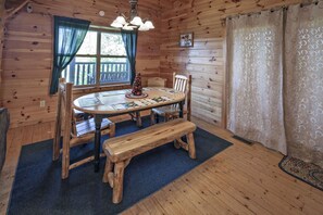 A wooden cabin interior with a round dining table, wooden chairs, a bench, a chandelier, a Christmas tree, and a window with curtains. - Bear Hugs - Great Cabin! 2 Bedroom Cabin by RedAwning (Sevierville)