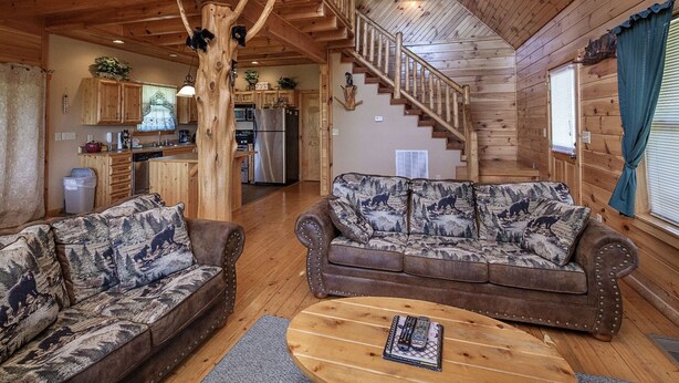 A cozy cabin interior with a wooden staircase, a kitchen area, and two patterned sofas. - Bear Hugs - Great Cabin! 2 Bedroom Cabin by RedAwning (Sevierville)