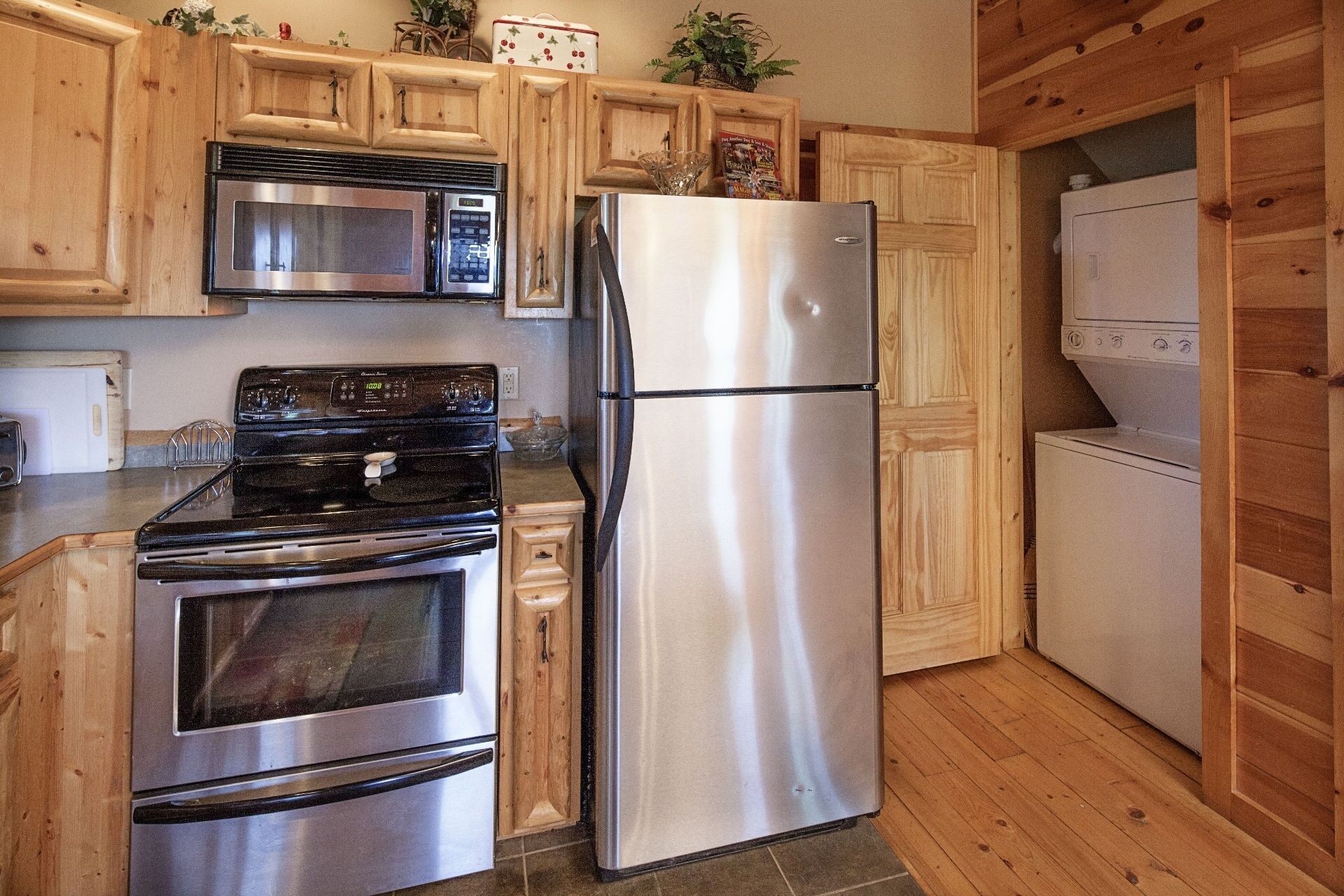 A kitchen with wooden cabinets, stainless steel appliances including a microwave, oven, and refrigerator, and a washing machine.