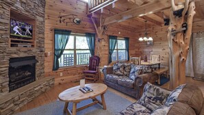 A cozy cabin interior with a stone fireplace, wooden walls, a sofa set, and a dining table. - Bear Hugs - Great Cabin! 2 Bedroom Cabin by RedAwning (Sevierville)