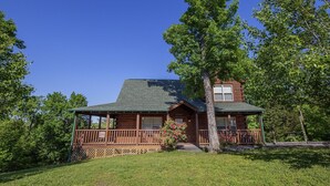A log cabin with a porch, a chimney, and a small garden area. - Bear Hugs - Great Cabin! 2 Bedroom Cabin by RedAwning (Sevierville)