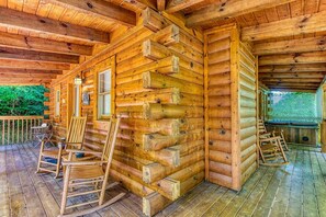 A log cabin with a porch, rocking chairs, and a ladder.