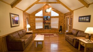 A cozy log cabin interior with a fireplace, two leather sofas, a wooden coffee table, and a ceiling fan. - Er79 - Robyn's Nest - Great Location. Close To All The Action! 2 Bedroom Cabin by RedAwning (Pigeon Forge)