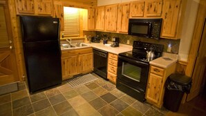 A compact kitchen with wooden cabinets, a black refrigerator, a microwave, a stove, and a sink. - Er79 - Robyn's Nest - Great Location. Close To All The Action! 2 Bedroom Cabin by RedAwning (Pigeon Forge)