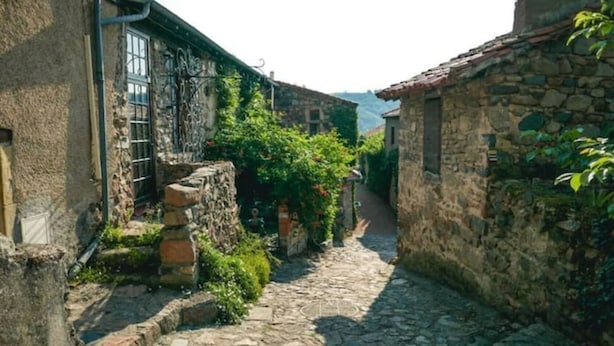 Une ruelle étroite pavée, bordée d’immeubles en pierre dont les fenêtres et les portes sont bien visibles.