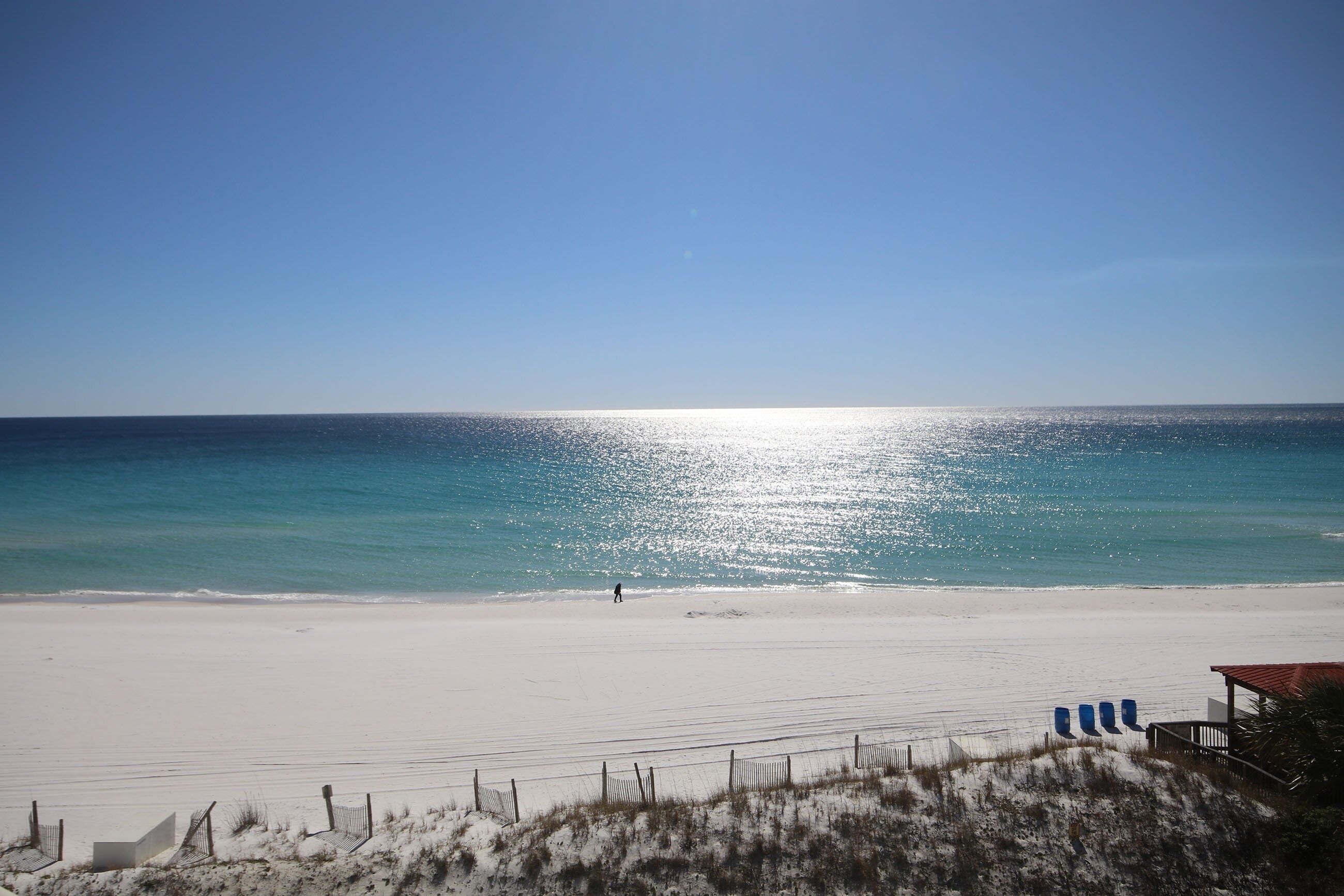 A beach with a clear sky, a sandy shore, and a few chairs along the edge.