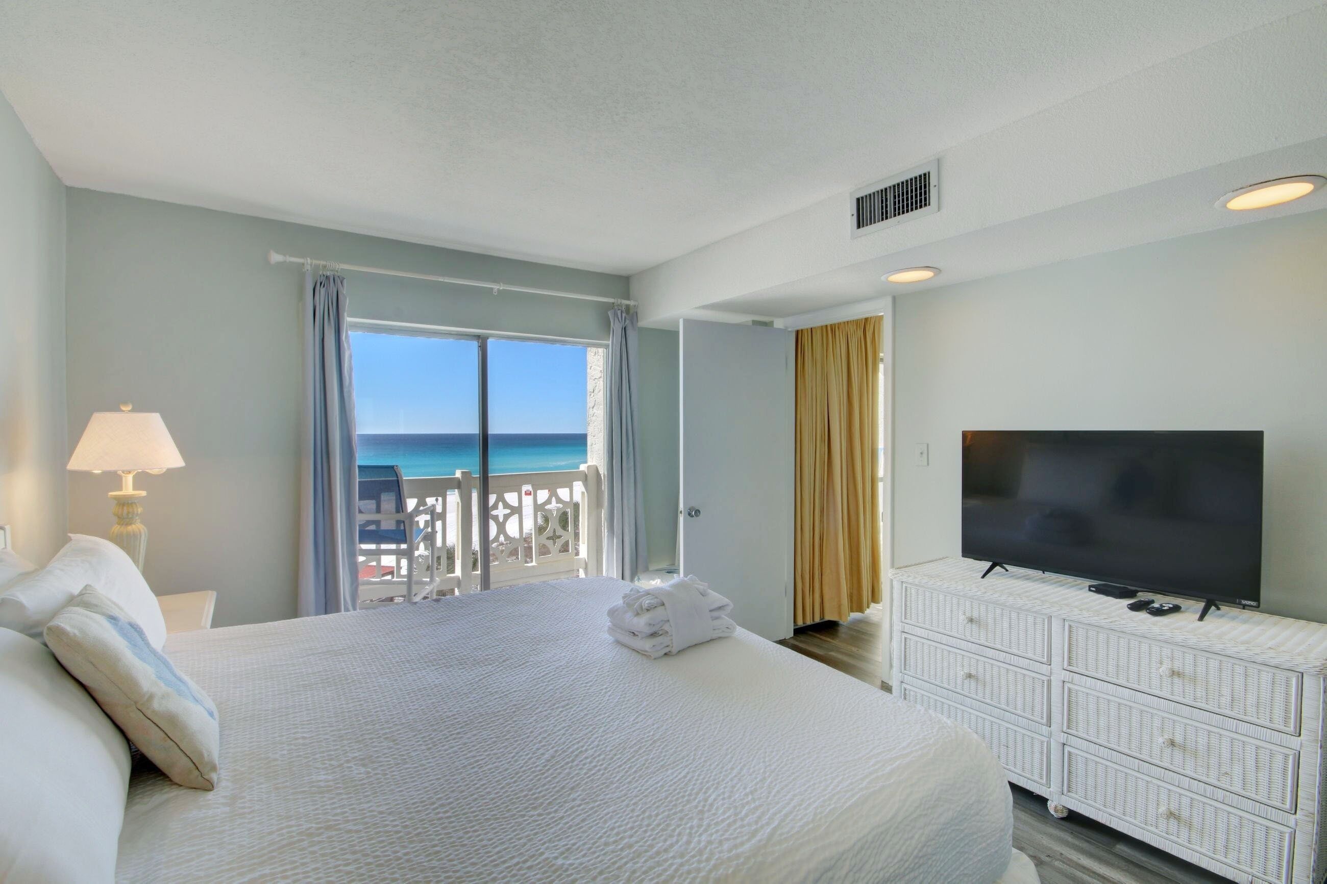 A hotel room with a bed, a TV, a balcony with a view of the sea, and a white dresser.