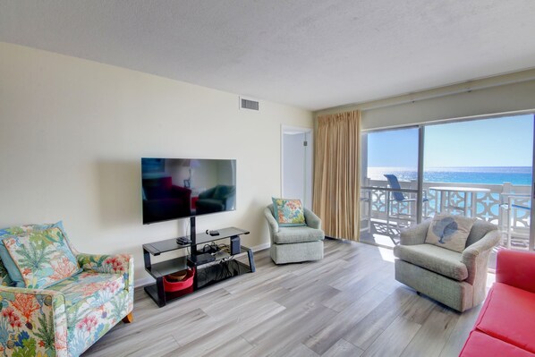 Una sala de estar con un televisor de pantalla plana, dos sillones, un sofá rojo y un balcón con vista al mar.