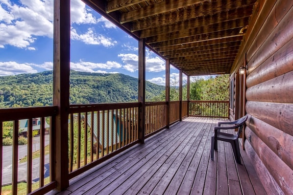 A wooden deck with a bench, overlooking a forested mountain range.