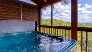 A hot tub with a wooden deck and a view of a forested landscape.