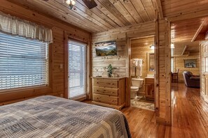 A wooden cabin bedroom with a bed, dresser, and a bathroom visible through an open door. - Ern864 - The Cedars - Great Location! Close To All The Action! 5 Bedroom Cabin by RedAwning (Pigeon Forge)