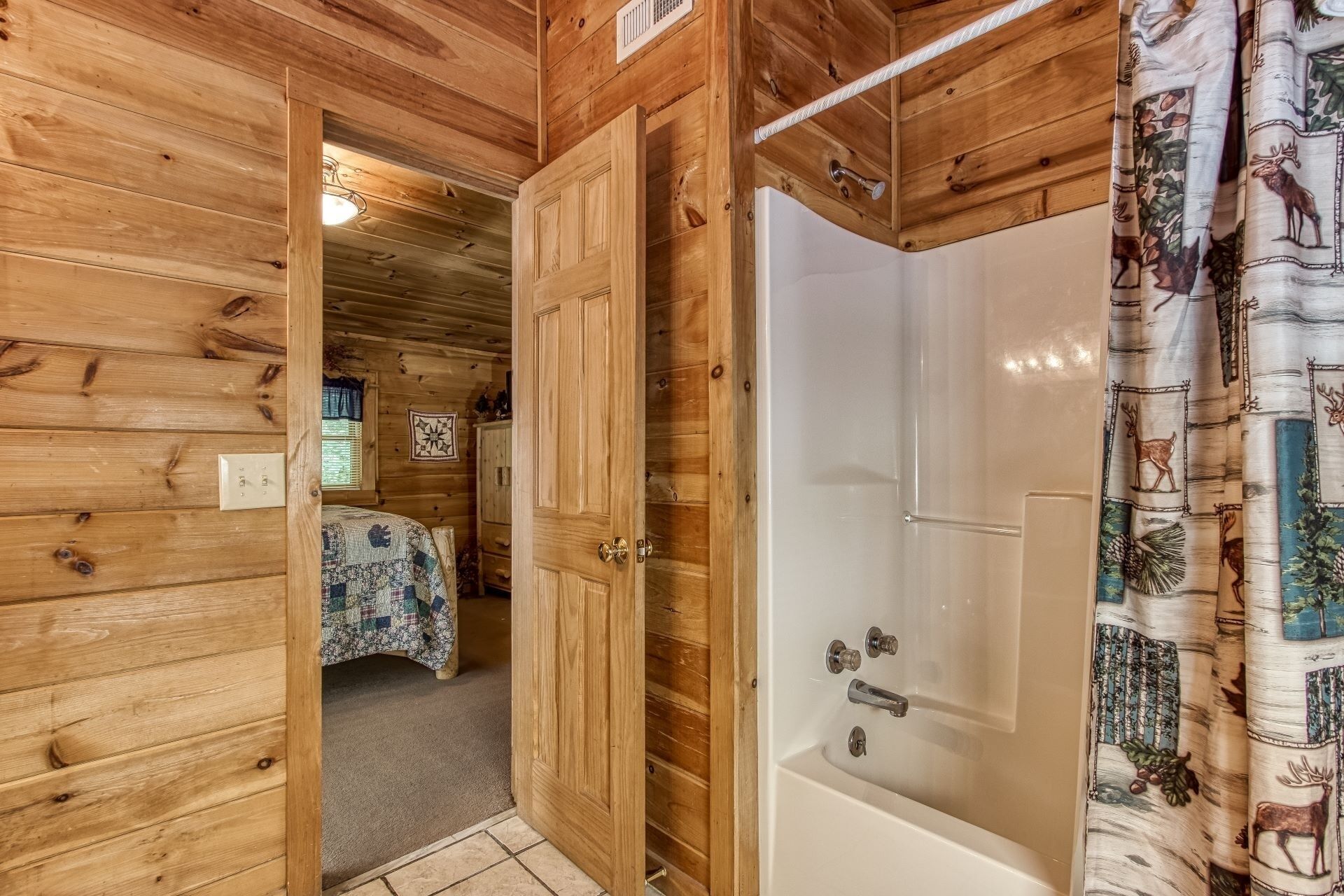 A wooden cabin interior with a bathroom featuring a shower and a bed with a checkered blanket.
