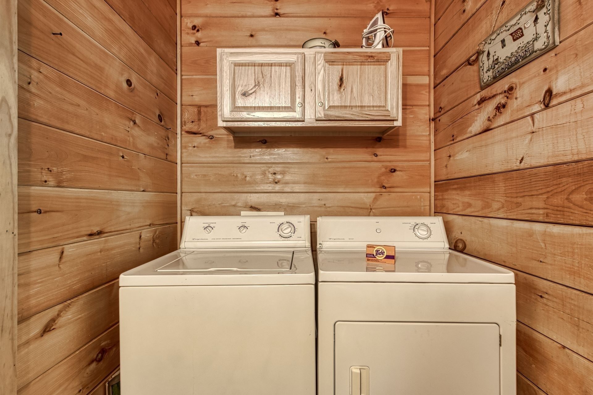 Une buanderie avec deux lave-linge et deux sèche-linge blancs, des murs en bois et un petit placard au-dessus des appareils.