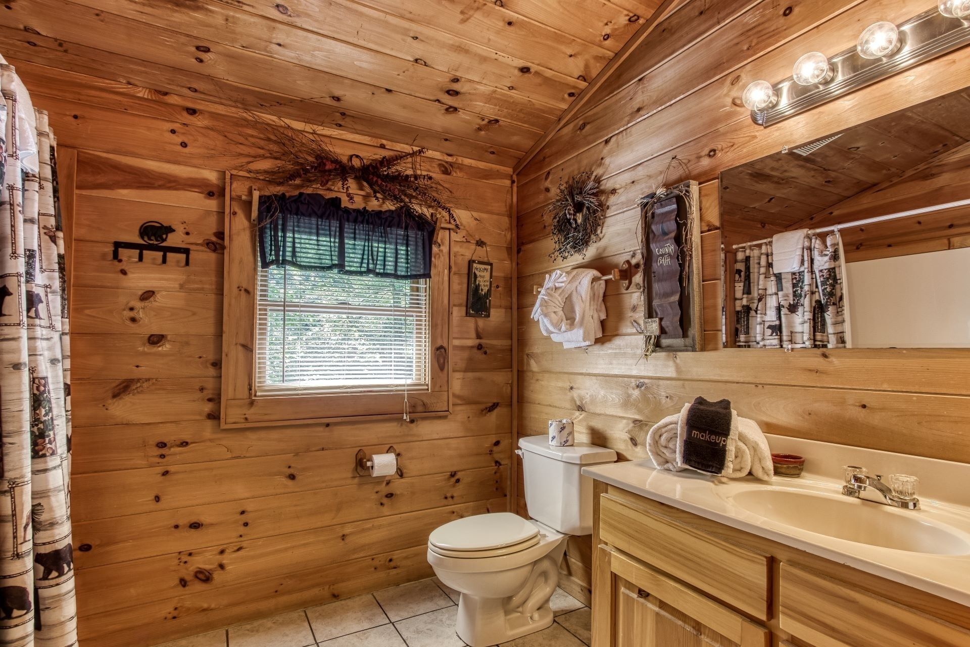 A wooden cabin bathroom with a toilet, sink, and window.