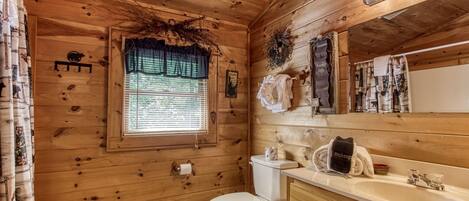 A wooden cabin bathroom with a toilet, sink, and window.
