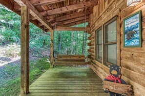 A wooden cabin with a porch, a bench, a welcome sign, and a bear decoration. - Mystic Mountain - Great Location! Close To All The Action! 2 Bedroom Cabin by RedAwning (Pigeon Forge)