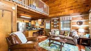 A cozy cabin interior with a wooden ceiling, a kitchen area, a living room with a sofa and coffee table, and a balcony with a railing. - Er17 - The Perfect Getaway Great Location - Close To Town! 1 Bedroom Cabin by RedAwning (Pigeon Forge)