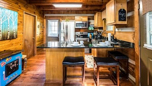 A cozy cabin-style kitchen with wooden walls, a central island with stools, and modern appliances. - Er17 - The Perfect Getaway Great Location - Close To Town! 1 Bedroom Cabin by RedAwning (Pigeon Forge)
