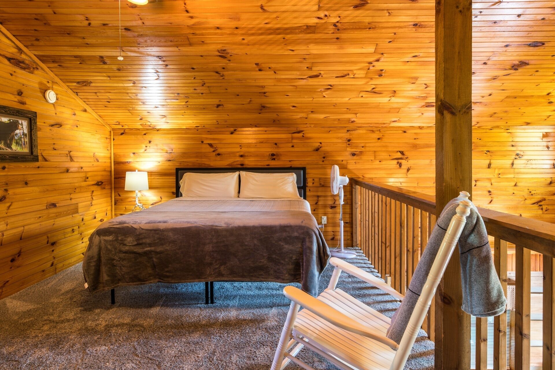 A cozy wooden cabin bedroom with a bed, a nightstand, a lamp, and a chair.