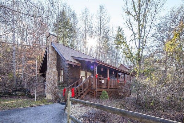 A rustic cabin with a stone chimney, wooden deck, and a staircase leading to the entrance. - Er38b - Grandma's Hideaway - Great Location! Close To Town 1 Bedroom Cabin by RedAwning (Pigeon Forge)