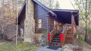 A rustic cabin with a stone chimney, wooden exterior, and a covered porch with red decorations.