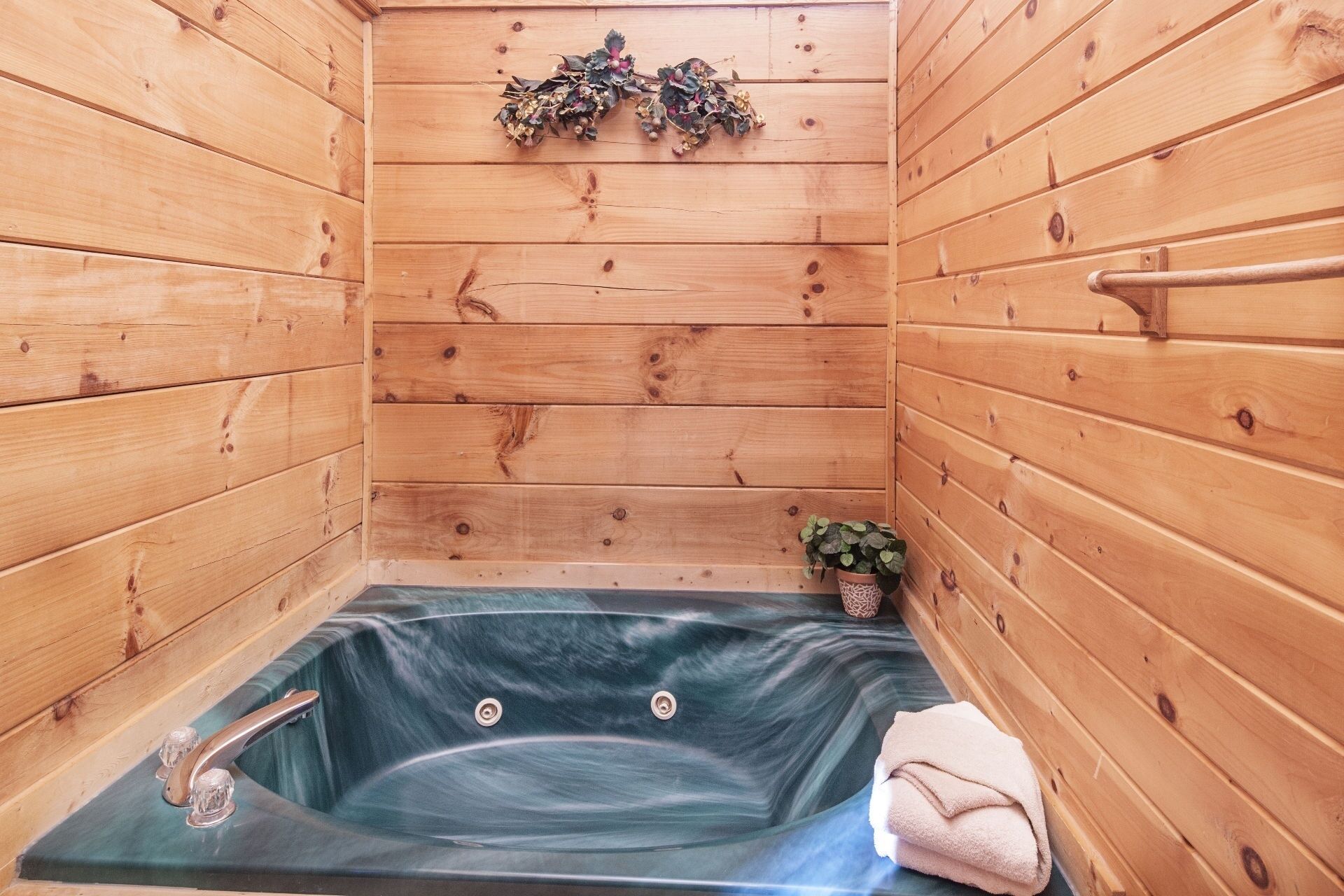 Una sauna de madera con una bañera de hidromasaje envuelta en cristal, una pequeña planta en maceta y una toalla en el suelo.