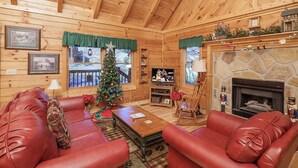 A cozy log cabin interior with leather sofas, a Christmas tree, a fireplace, and a television.