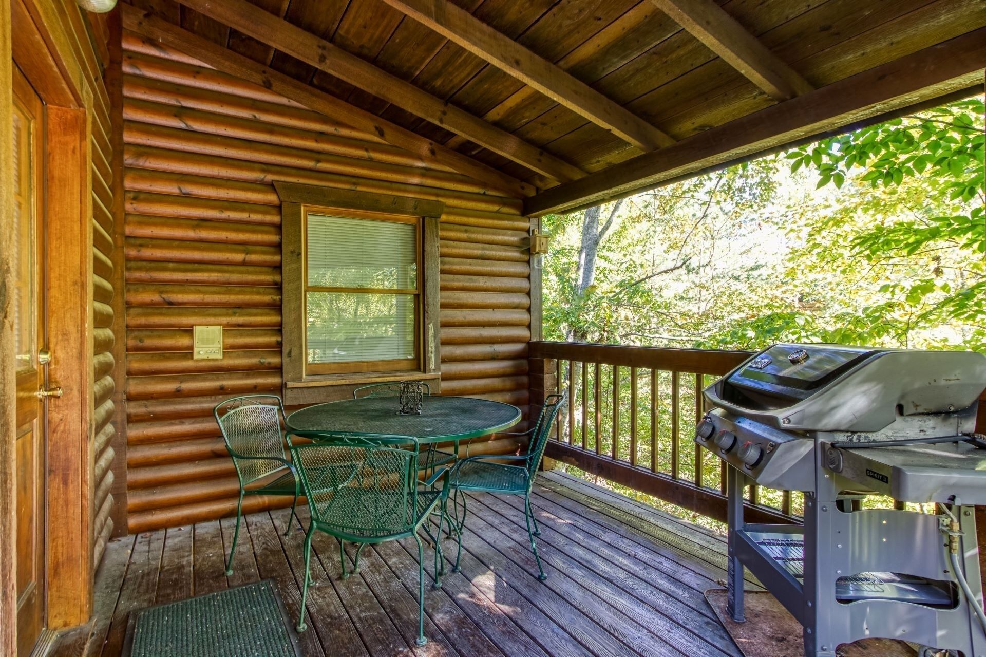 A wooden cabin with a covered porch, a table with chairs, and a grill.