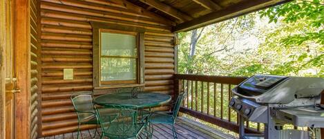 A wooden cabin with a covered porch, a table with chairs, and a grill.