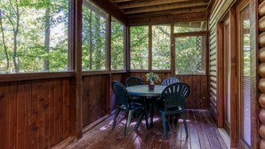 A wooden deck with a table and chairs, surrounded by large windows offering a view of trees. - Er19 - Fryemont Great Location - Close To Town! 3 Bedroom Cabin by RedAwning (Pigeon Forge)