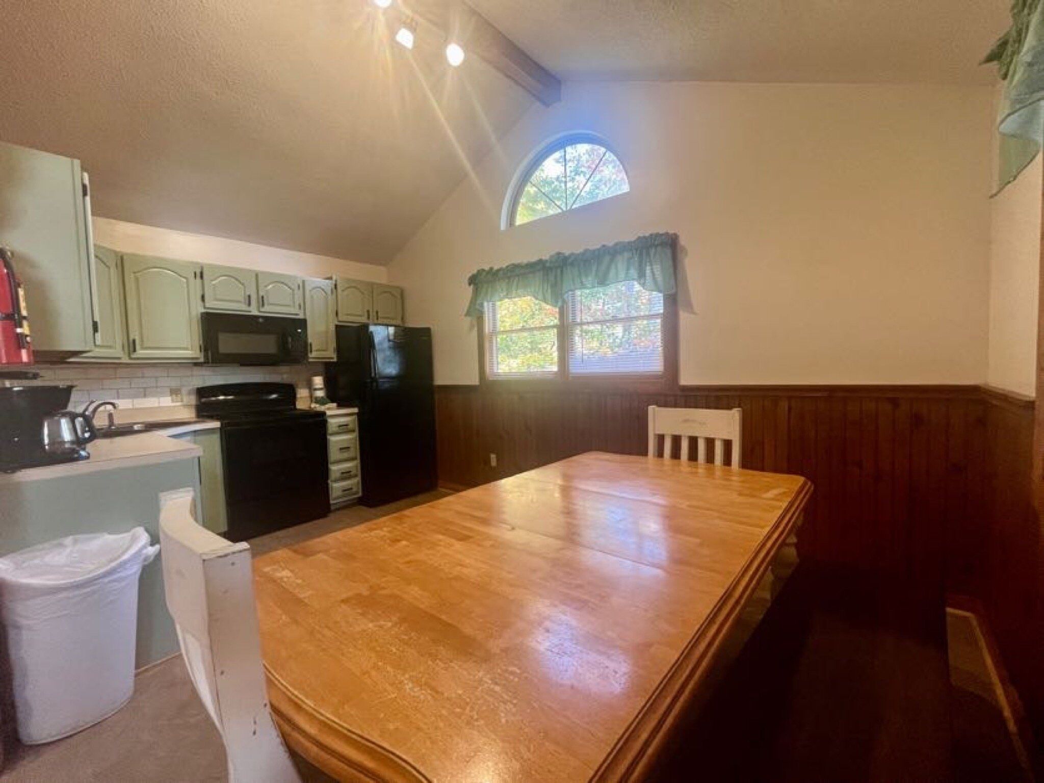 A compact kitchen with a wooden table, a microwave, a refrigerator, and a window with a view of greenery.