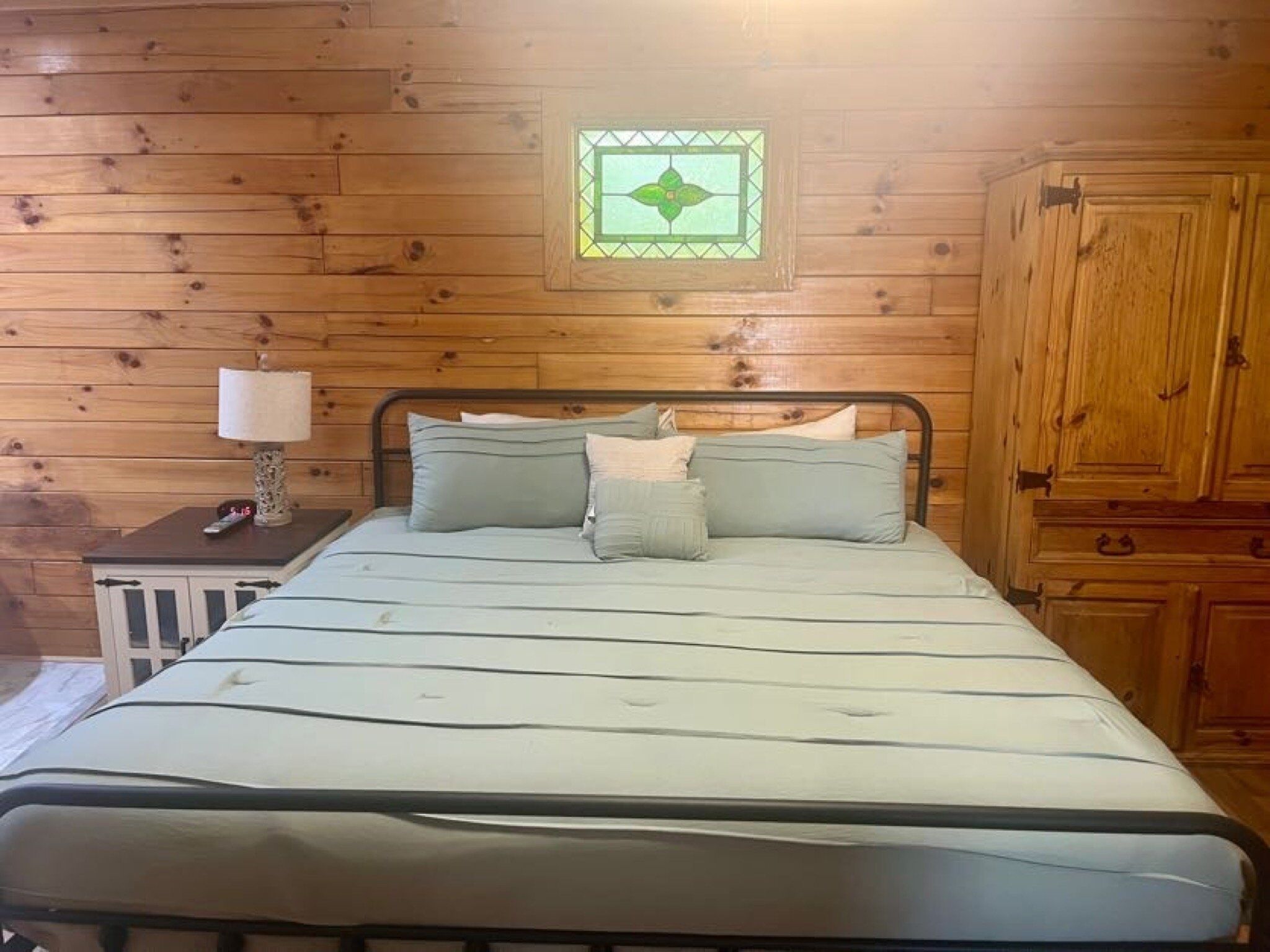 A wooden-paneled room with a bed, a nightstand, a lamp, and a cabinet.