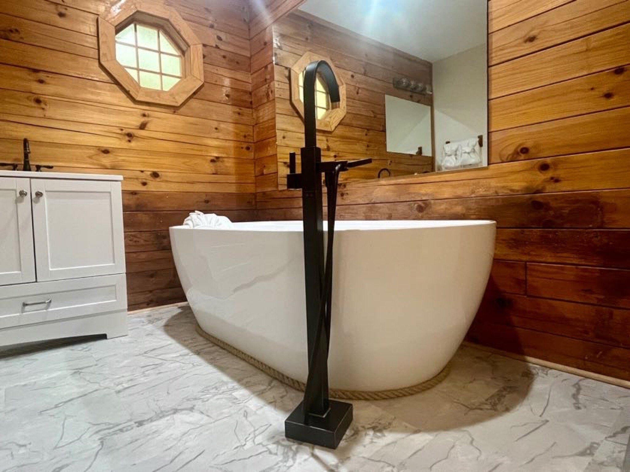 L’intérieur d’un chalet en bois est doté d’une grande baignoire sur pieds, d’un meuble blanc et d’un plafond en bois agrémenté d’une fenêtre hexagonale.