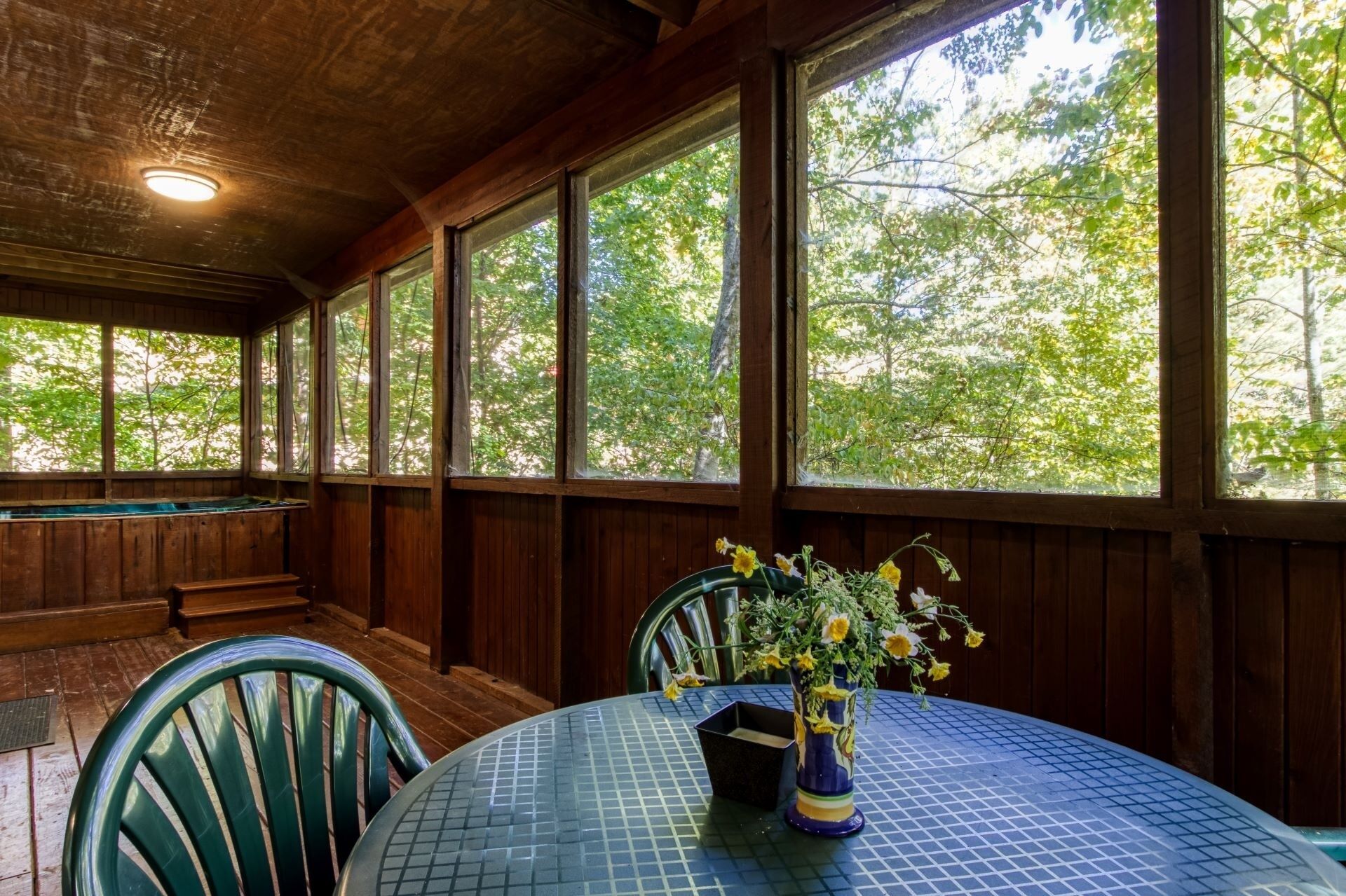 A covered patio with a table and chairs, large windows, and a ceiling light.