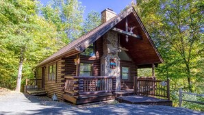 A log cabin with a stone chimney, wooden deck, and a covered porch. - Er19 - Fryemont Great Location - Close To Town! 3 Bedroom Cabin by RedAwning (Pigeon Forge)