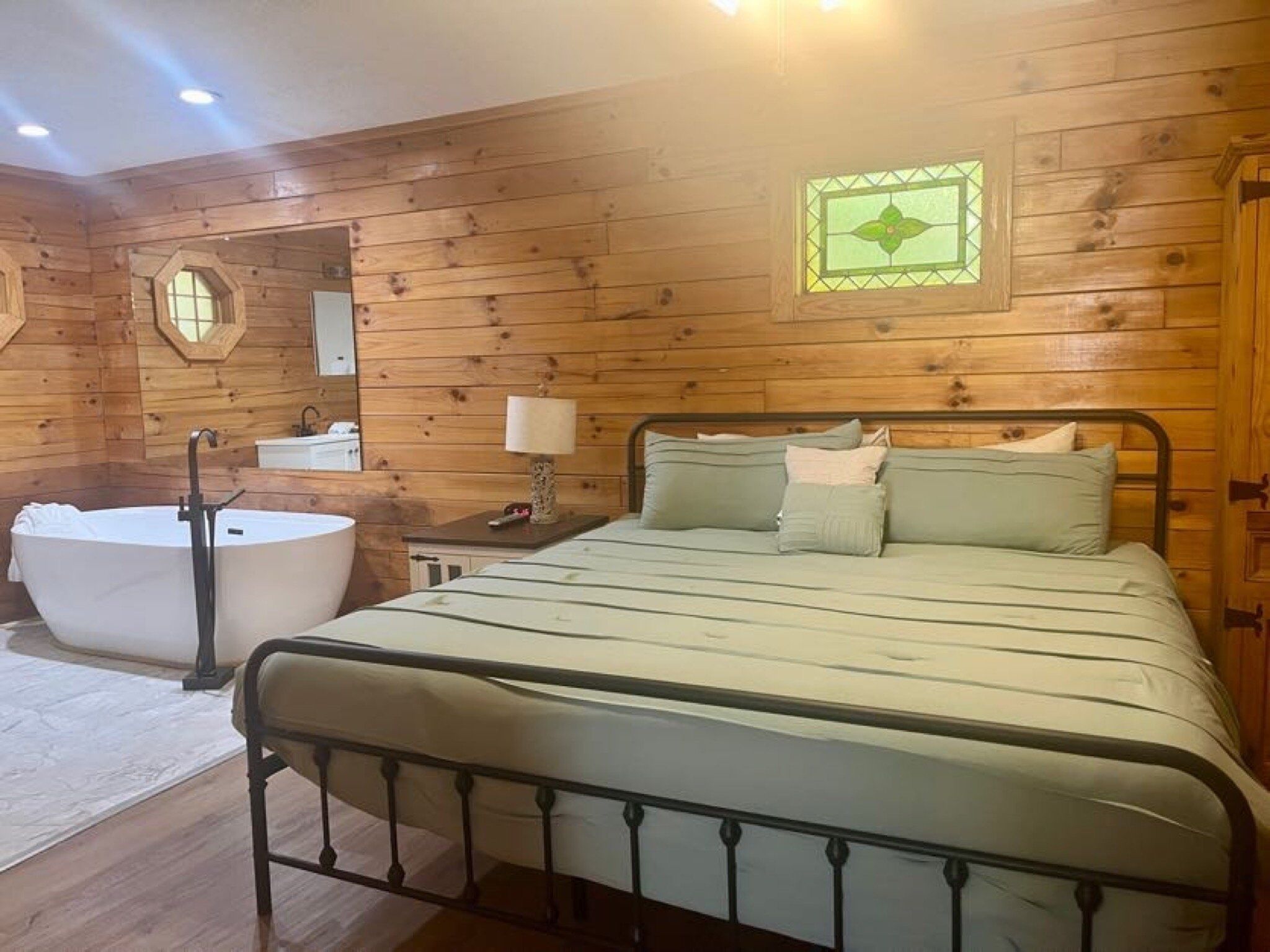 Un dormitorio tipo cabaña de madera con una cama grande, un baño separado con bañera y un tocador pequeño con espejo.