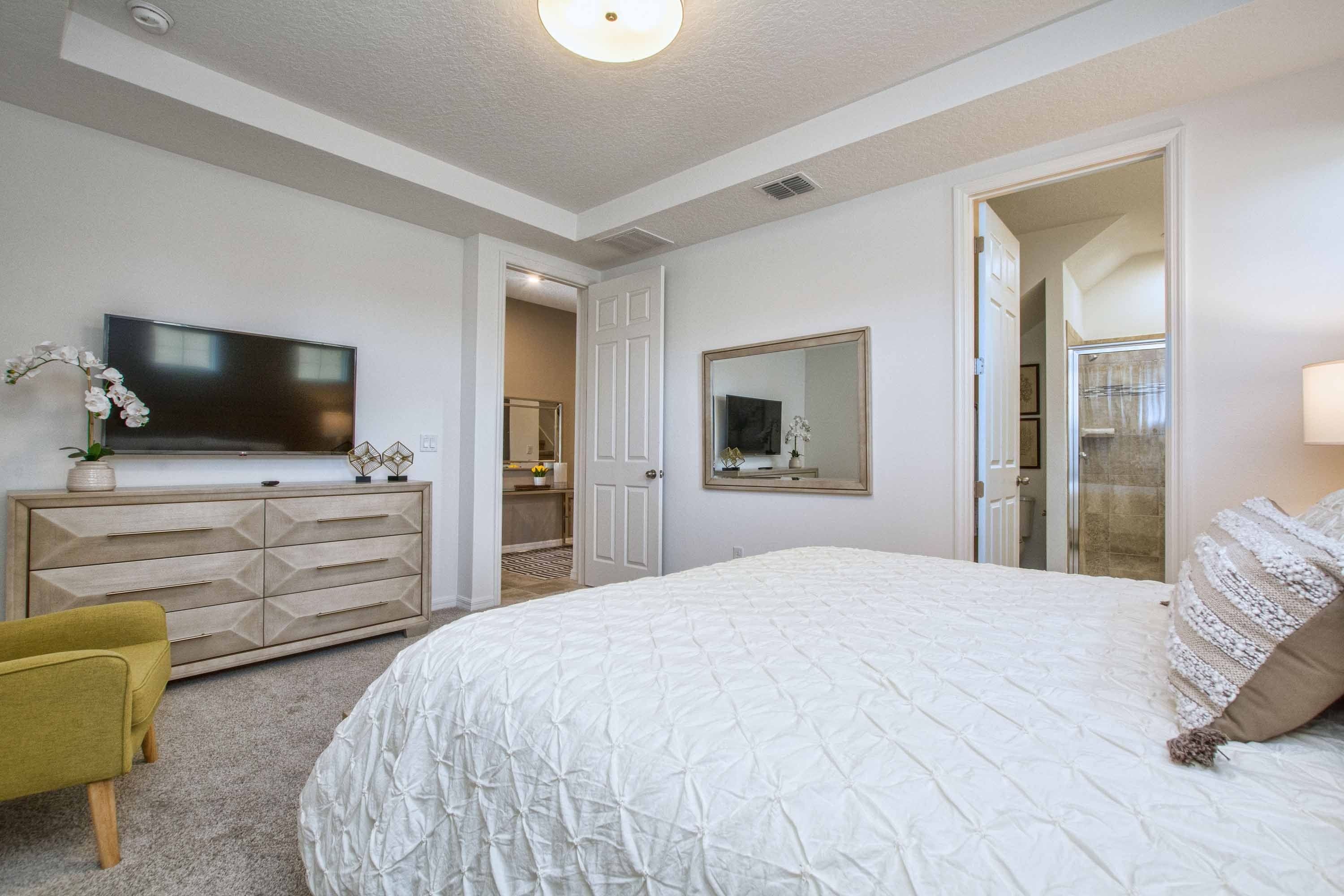 Quarto com cama, penteadeira, televisão e espelho.