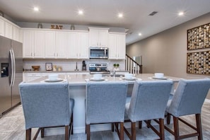 A modern kitchen with white cabinets, a central island with bar stools, and a stainless steel refrigerator.