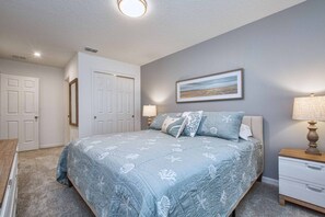 A bedroom with a bed, a nightstand, a lamp, a framed picture on the wall, and a door.