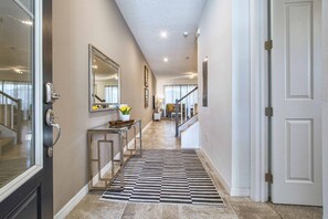 A hallway with a checkered rug, a mirror, a door, and a staircase leading to another room.