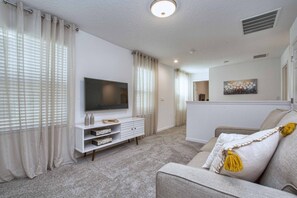 A living room with a flat-screen TV, a white console table, and a beige sofa with a yellow tassel pillow.