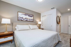 A bedroom with a bed, two bedside tables, a wall-mounted painting, a door, and a mirror.