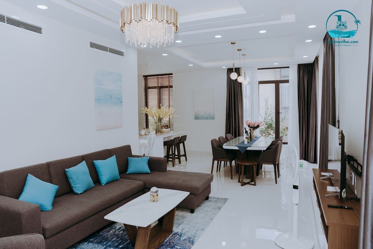 A modern living room with a brown sectional sofa, a white coffee table, and a dining area with a wooden table and chairs.