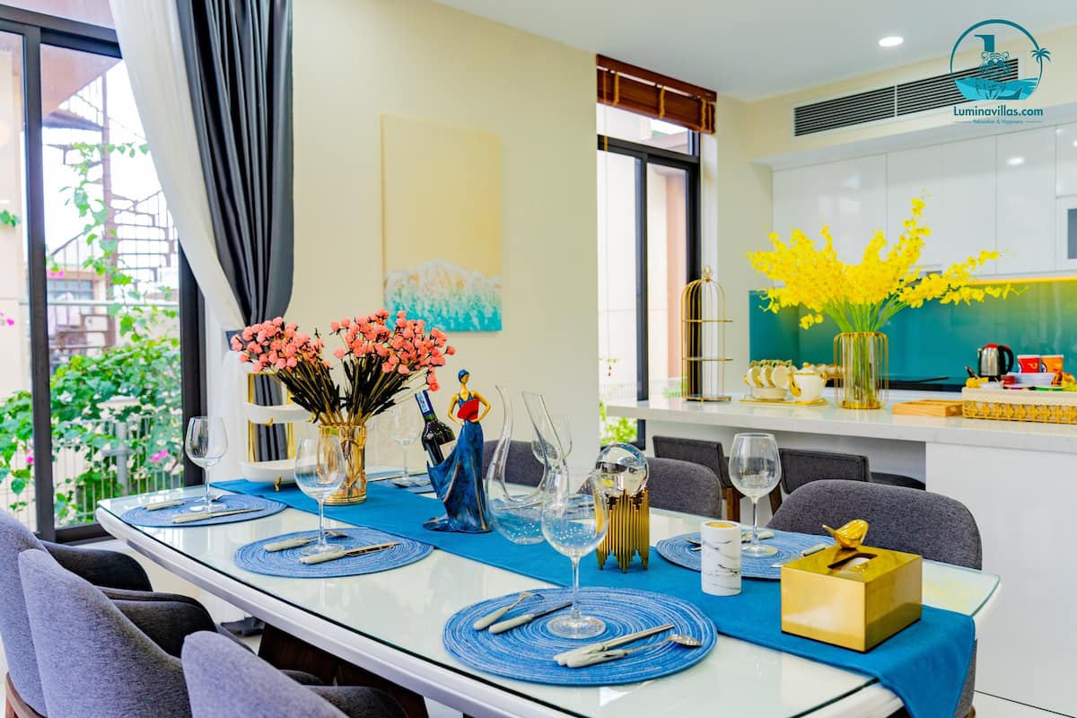 A dining table set with blue placemats, clear glassware, and a vase with yellow flowers.