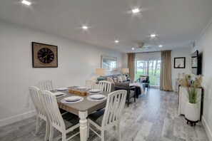 Un comedor con una mesa de madera dispuesta para cuatro personas, sillas blancas y un reloj en la pared.
