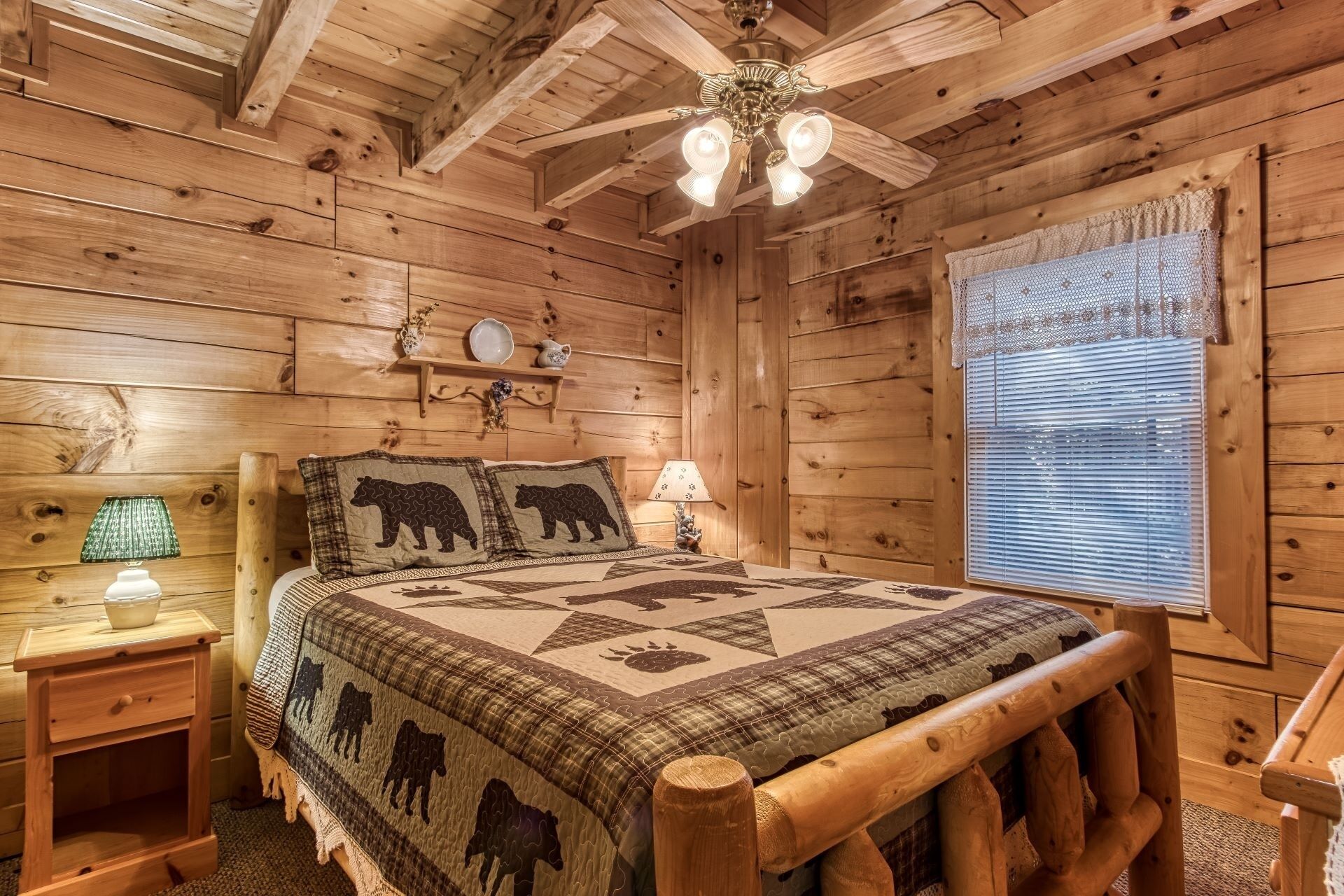 A cozy wooden cabin bedroom with a bed, two nightstands, a ceiling fan, and a window with blinds.